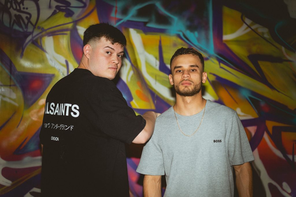 The duo in front of a painted graffiti wall.